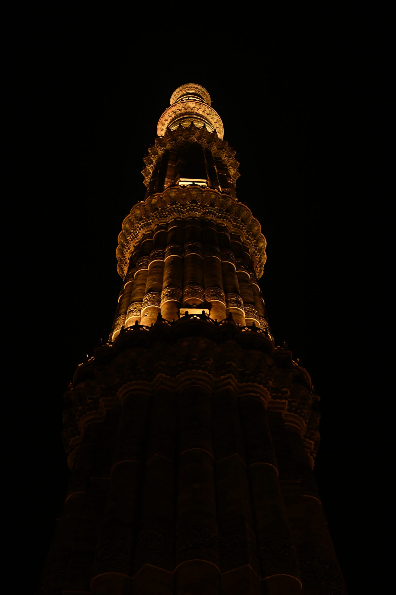 Illuminated Qutub Minar photographed at night against a dark sky in New Delhi, India.